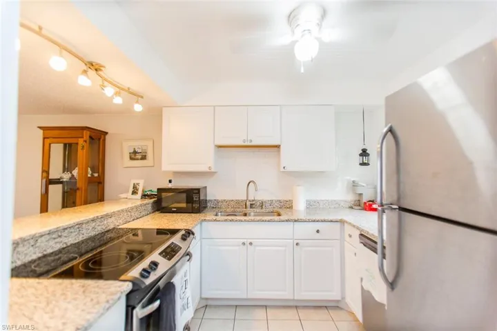Kitchen featuring electric stove, a sink, white cabinetry, freestanding refrigerator, and black microwave