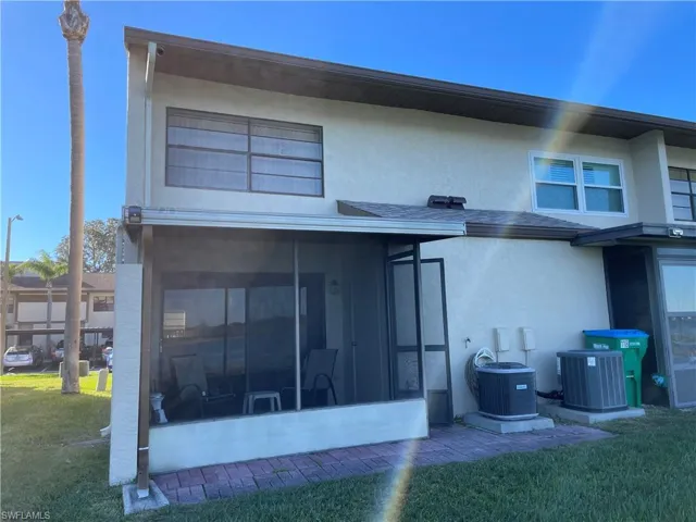 Back of house featuring a sunroom, a lawn, central AC, and stucco siding