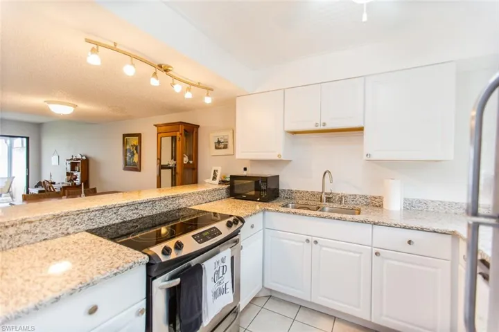 Kitchen with black microwave, light tile patterned floors, stainless steel range with electric stovetop, white cabinets, and a sink