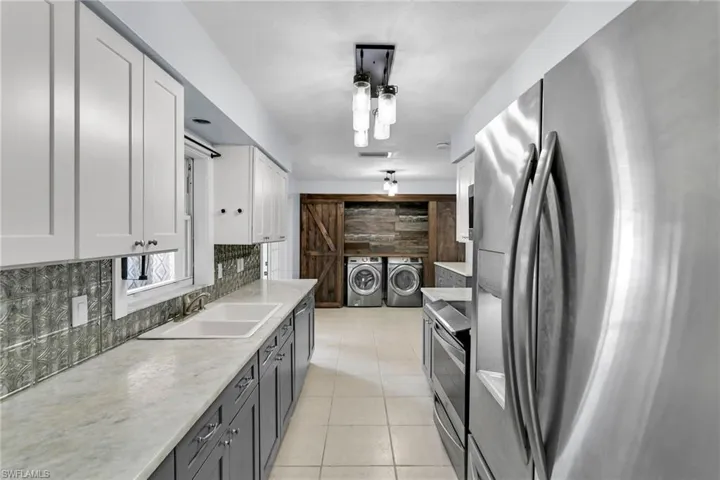 Kitchen with white cabinetry, sink, a barn door, washer and dryer, and appliances with stainless steel finishes