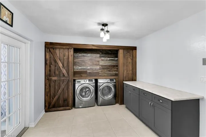 Clothes washing area featuring cabinets, light tile patterned floors, and washer and clothes dryer
