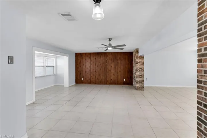 Unfurnished living room with light tile patterned flooring, ceiling fan, and wood walls
