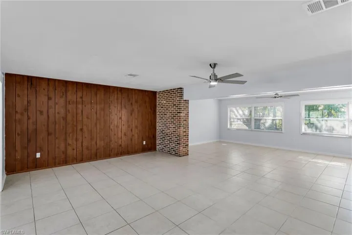 Unfurnished living room featuring wood walls, a fireplace, ceiling fan, and light tile patterned floors