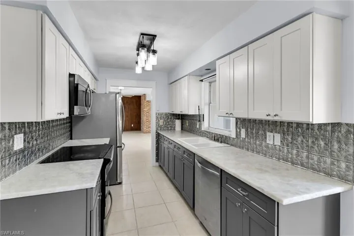 Kitchen featuring backsplash, stainless steel appliances, sink, white cabinets, and light tile patterned flooring
