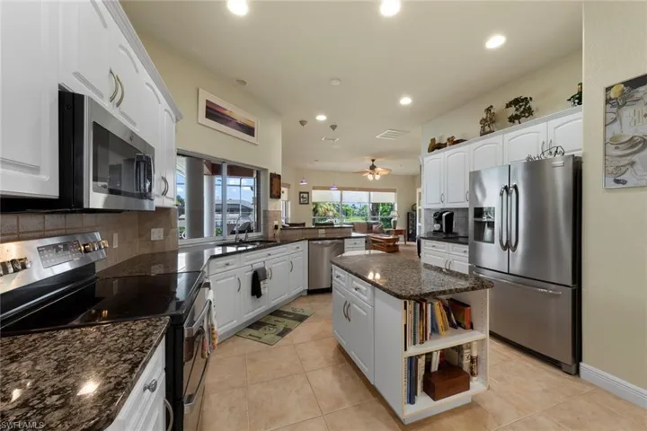 Kitchen featuring stainless steel appliances, dark stone counters, kitchen peninsula, ceiling fan, and tasteful backsplash