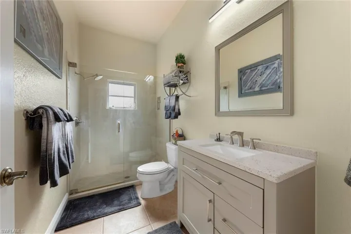 Bathroom featuring tile patterned flooring, toilet, a shower with door, and vanity