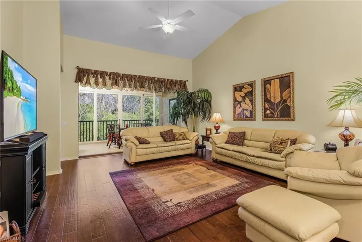 Living room with dark hardwood / wood-style floors, ceiling fan, and high vaulted ceiling