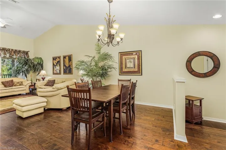 Dining space featuring dark hardwood / wood-style floors, ceiling fan with notable chandelier, and vaulted ceiling