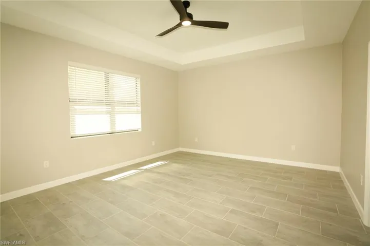 Spacious room featuring a tray ceiling with a ceiling fan, light wood-finish plank tile flooring, and a large window with horizontal blinds