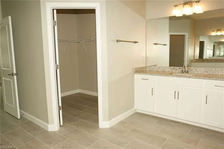 Bathroom featuring a double vanity with granite countertop, white cabinetry, and brushed nickel hardware