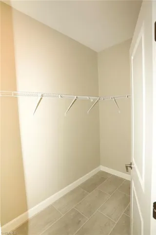 Walk-in closet with neutral-toned walls, white wire shelving, baseboard trim, and rectangular tile flooring