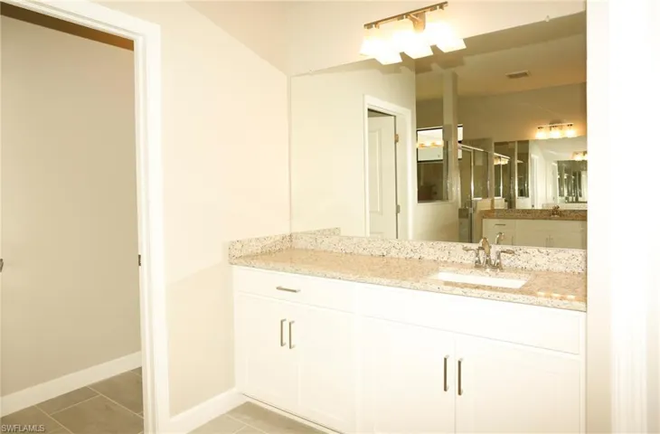 Bathroom vanity featuring a light-colored granite countertop, an undermount sink with a chrome faucet, and white cabinetry