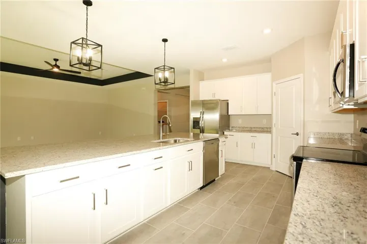 Open-concept kitchen featuring an oversized island with an undermount sink, pendant lighting, stainless steel appliances, white cabinetry, and granite countertops