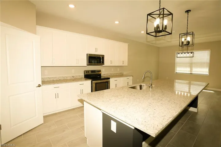 Spacious kitchen featuring an expansive island with an undermount sink, white cabinetry, integrated stainless steel appliances, and tile flooring