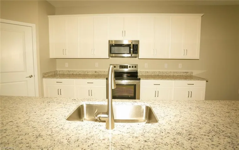 Spacious kitchen featuring an undermount stainless steel sink, brushed nickel faucet, and a large granite countertop island