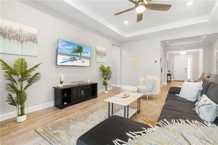 Living area with a tray ceiling, wood tiled floors, recessed lighting, and a ceiling fan
