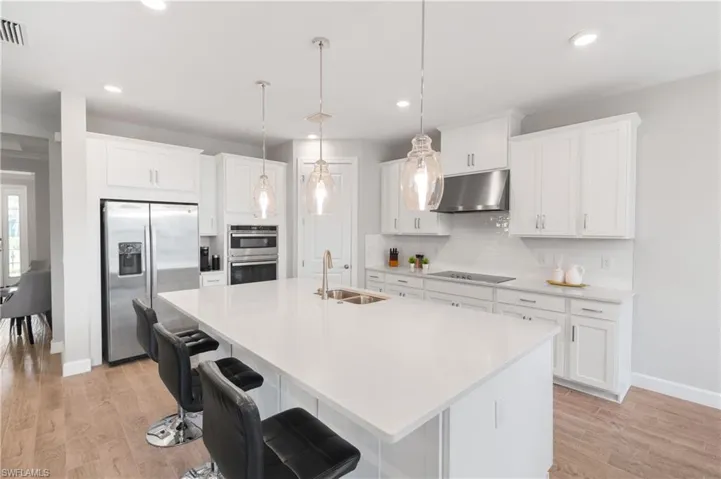 Kitchen featuring appliances with stainless steel finishes, a kitchen bar, decorative light fixtures, light wood finished floors, and white cabinetry
