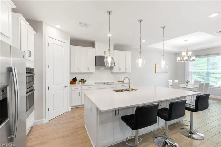 Kitchen featuring stainless steel appliances, a breakfast bar area, decorative backsplash, decorative light fixtures, and white cabinets