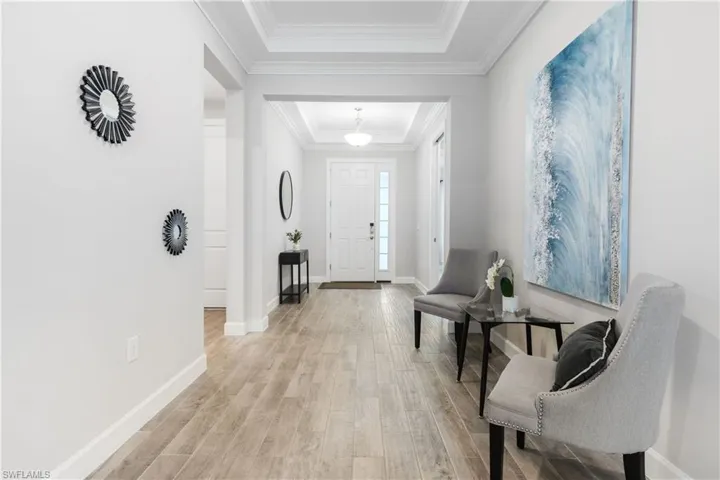 Foyer with a raised ceiling, light wood-style floors, and crown molding