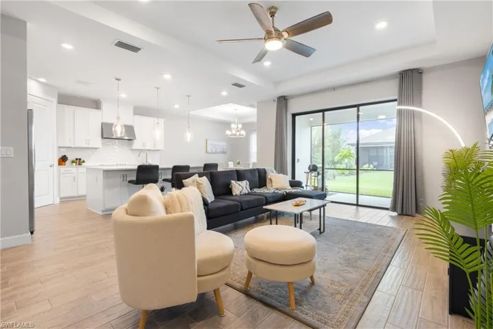 Living room featuring a chandelier, a tray ceiling, light wood-style floors, ceiling fan, and recessed lighting