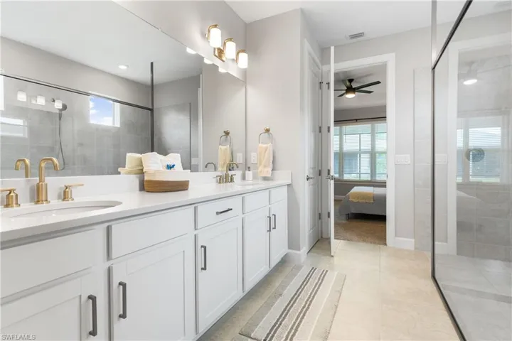 Ensuite bathroom featuring double vanity, a shower stall, light tile patterned floors, and a ceiling fan