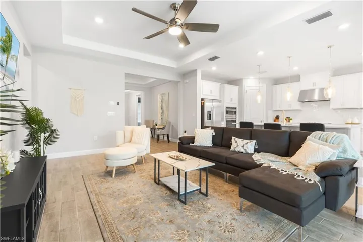 Living room with light wood-type flooring, a raised ceiling, a ceiling fan, and recessed lighting