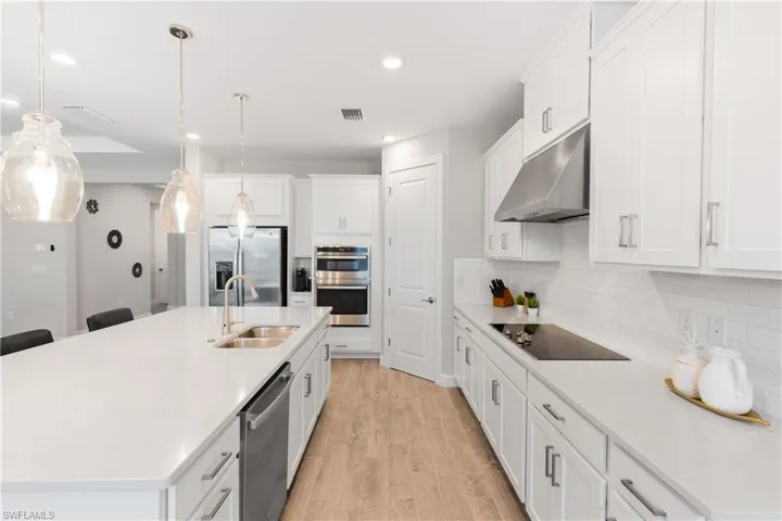 Kitchen featuring white cabinets, decorative light fixtures, a kitchen island with sink, under cabinet range hood, and stainless steel appliances
