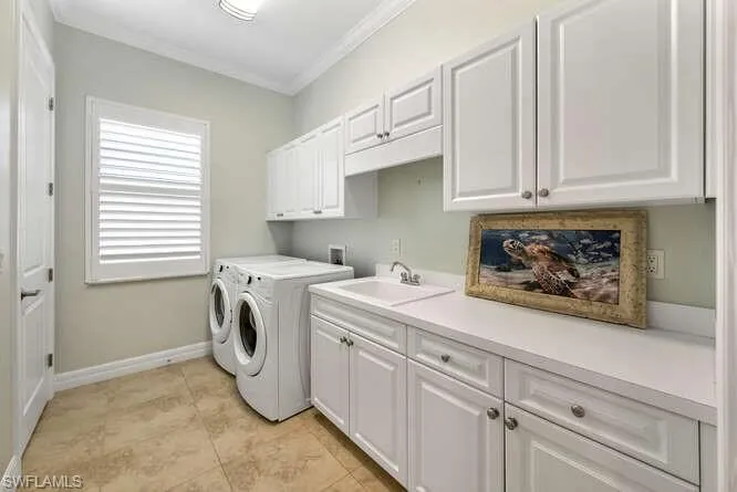 Main level Laundry area featuring washing machine and clothes dryer, sink, cabinets, and ornamental molding