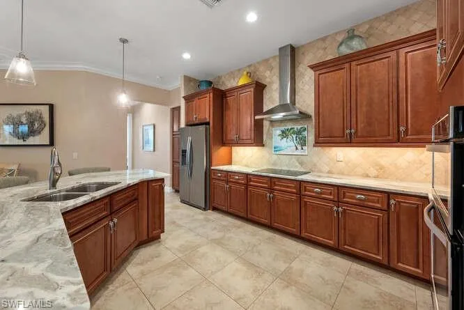 Kitchen with sink, hanging light fixtures, wall chimney exhaust hood, stainless steel fridge, and light stone countertops