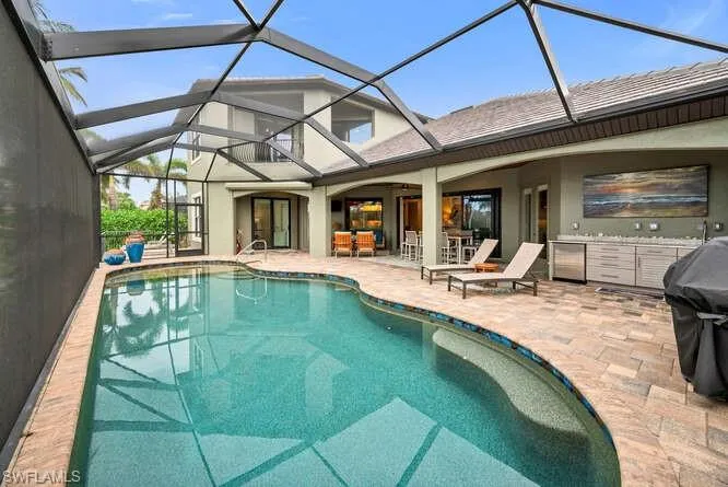 View of pool with glass enclosure, a patio area, and exterior kitchen
