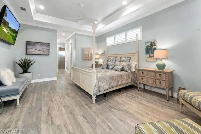 Main Level Primary Bedroom featuring ornamental molding, light hardwood / wood-style floors, ceiling fan, and a tray ceiling