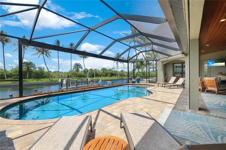 View of pool featuring glass enclosure, a water view, and a patio