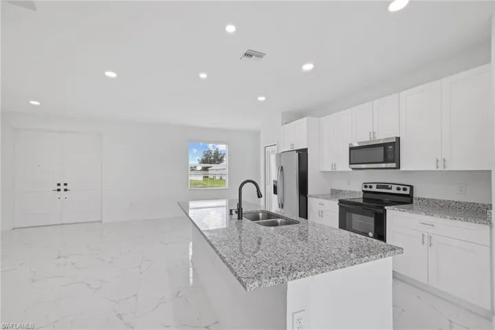 Kitchen featuring light tile patterned floors, light stone counters, a kitchen island with sink, appliances with stainless steel finishes, and sink