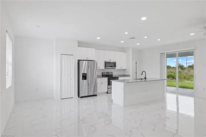 Kitchen with a kitchen island with sink, white cabinets, stainless steel appliances, and light tile patterned floors
