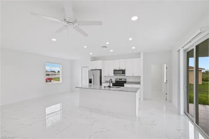 Kitchen featuring light tile patterned floors, a kitchen island with sink, ceiling fan, stainless steel appliances, and light stone countertops