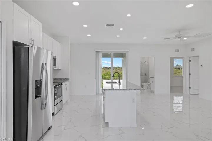 Kitchen with stainless steel fridge, range, light tile patterned floors, and a kitchen island with sink