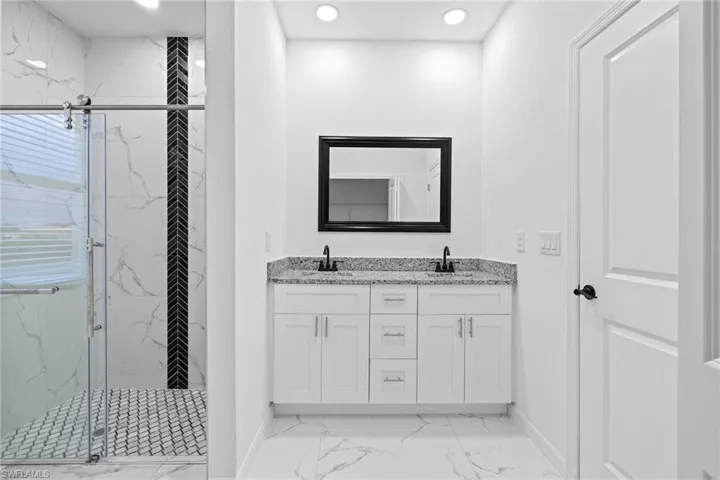 Bathroom featuring a shower with door, tile patterned floors, and dual bowl vanity