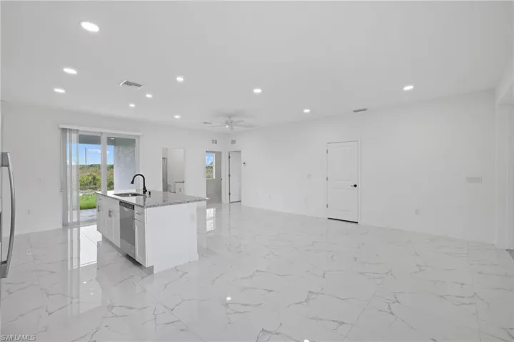 Kitchen featuring stainless steel dishwasher, light tile patterned flooring, white cabinets, sink, and a kitchen island with sink
