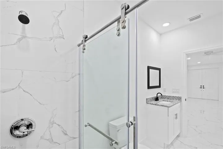 Bathroom featuring a shower with shower door, vanity, tile patterned flooring, and toilet