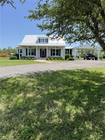View of front of home featuring a porch, a front lawn, board and batten siding, a carport, and gravel driveway