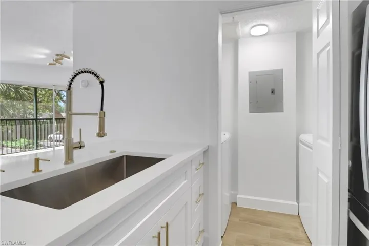 Kitchen with baseboards, electric panel, light countertops, white cabinets, and a sink