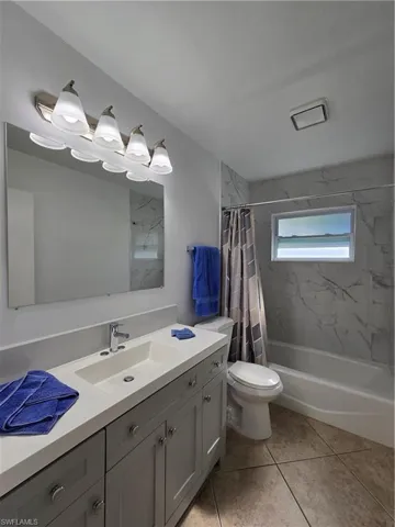 Full bathroom with shower / bathtub combination with curtain, toilet, vanity, and tile patterned floors