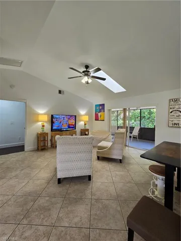 Tiled living room with ceiling fan and lofted ceiling with skylight