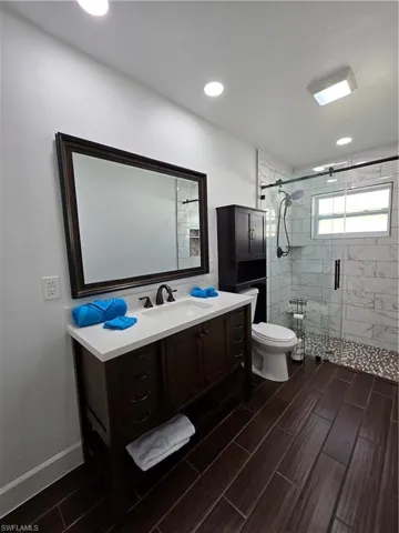 Bathroom featuring a shower with door, vanity, and toilet
