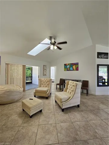 Tiled living room with ceiling fan and vaulted ceiling with skylight