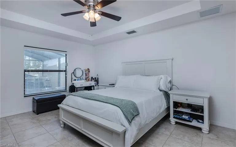 Bedroom featuring a tray ceiling with a ceiling fan, a large window with horizontal blinds, and ceramic tile flooring