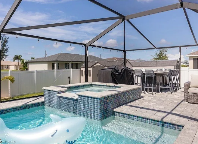 Screened outdoor space featuring a swimming pool, integrated spa with mosaic tile accents, and paver decking