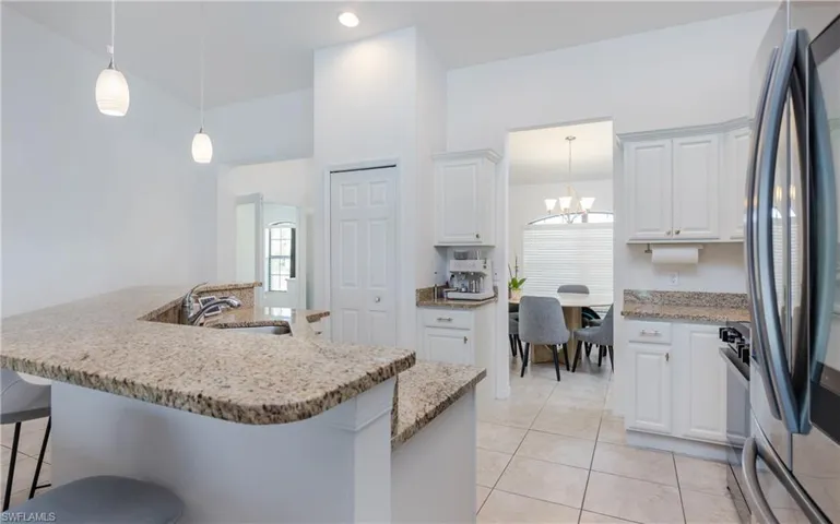 Kitchen featuring granite countertops, white cabinetry, stainless steel appliances, pendant lighting, and tiled flooring