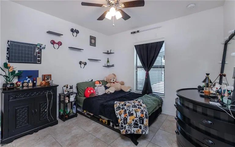 Bedroom featuring tile flooring, a window with blinds and drapes, a ceiling fan with integrated lighting, and multiple wall-mounted shelves