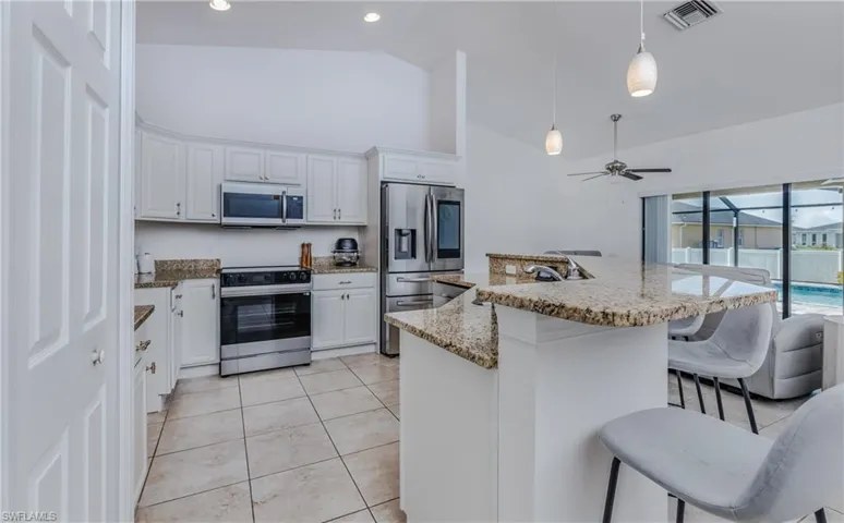 Open-concept kitchen featuring granite countertops, stainless steel appliances, white cabinetry, and tile flooring